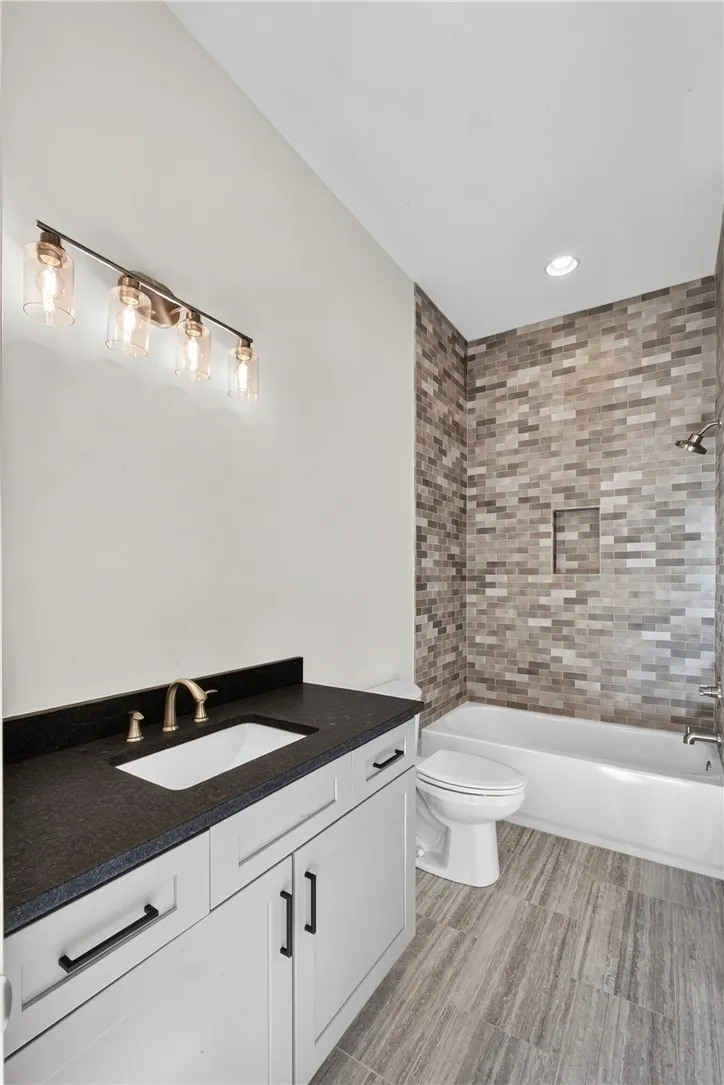 A well-appointed bathroom offers sleek white cabinetry, dark stone counters, and a modern tiled shower-tub combination.