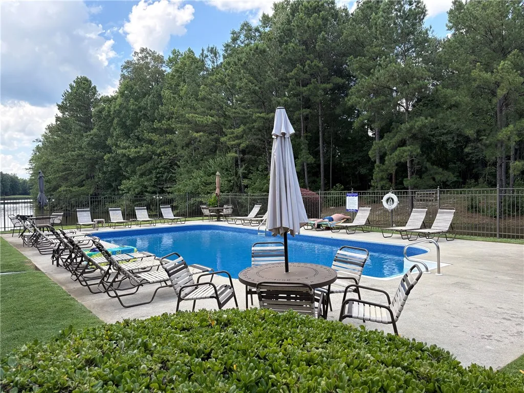 A sparkling outdoor pool awaits, nestled beside a tranquil lake with mature trees providing a natural backdrop.