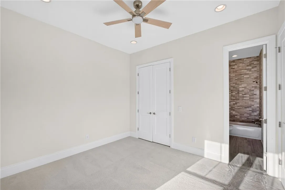 A well-lit bedroom features plush carpeting, a ceiling fan, and convenient access to an adjoining bathroom.