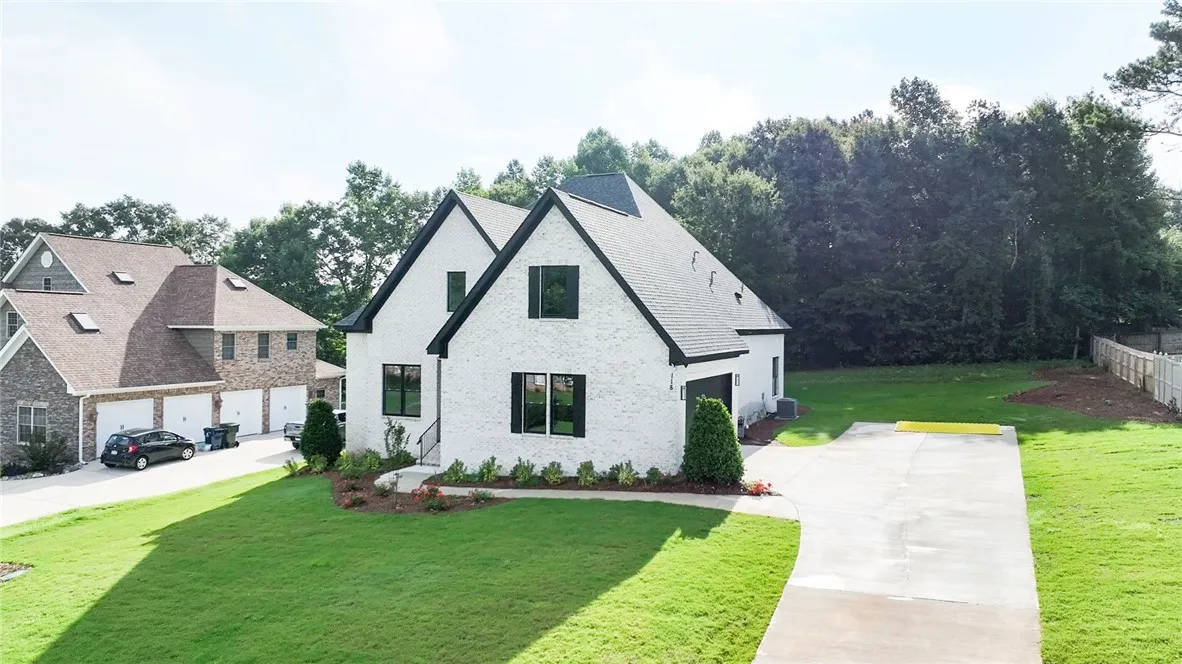 White brick home with black trim boasts a vibrant green lawn and a spacious driveway.