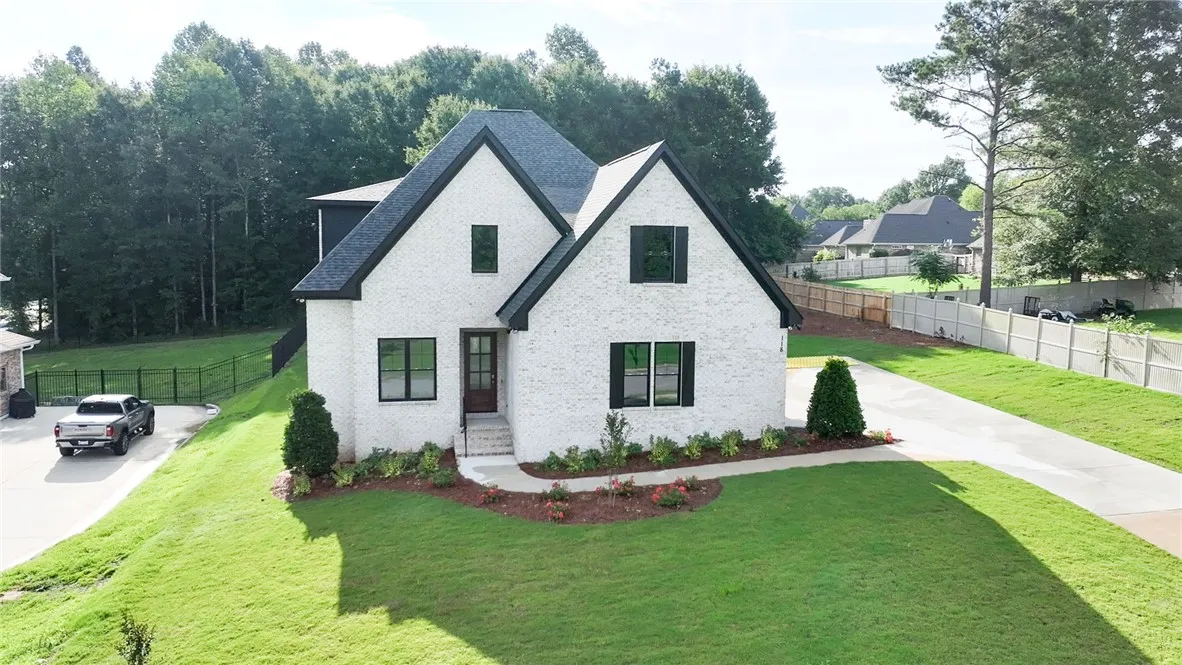 A striking white brick residence with a dark roofline offers classic charm and a generous front yard.