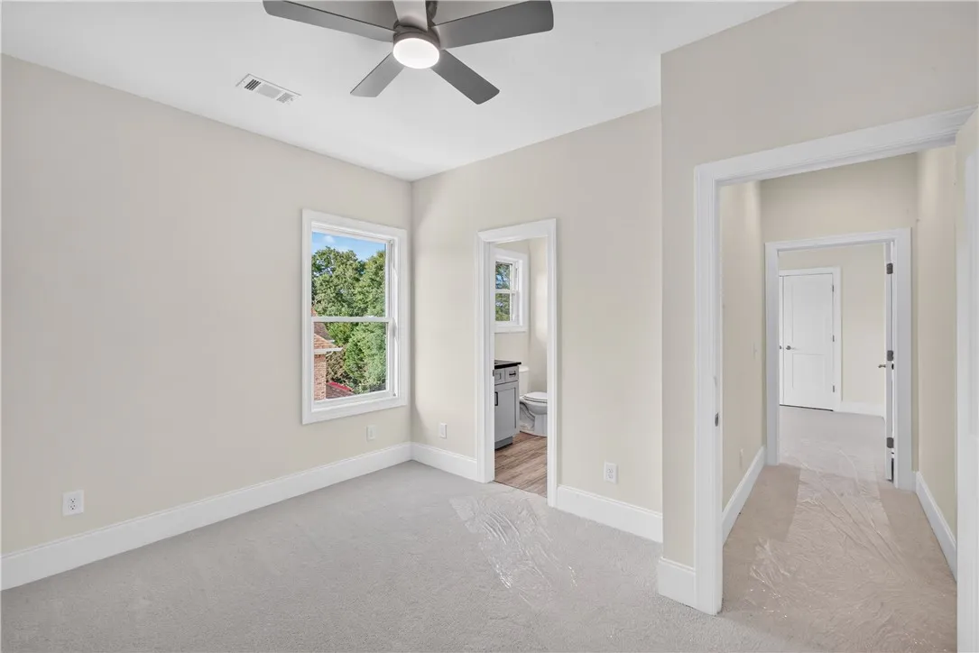 A well-lit bedroom features plush carpeting and a modern ceiling fan, with an adjacent bath.