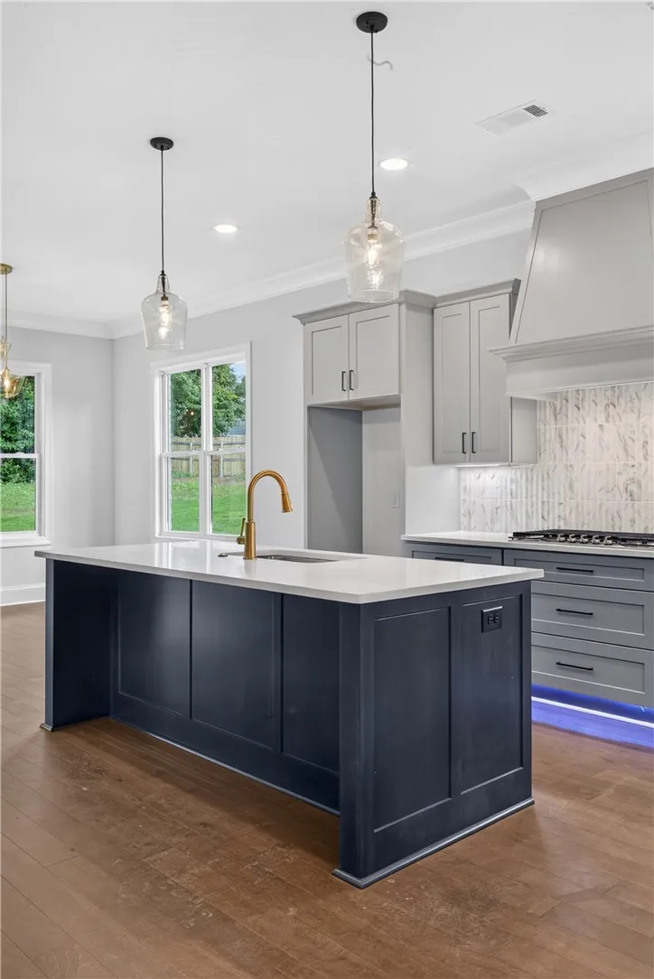 A contemporary kitchen features a spacious central island with a sink, golden faucet, and sleek pendant lighting.