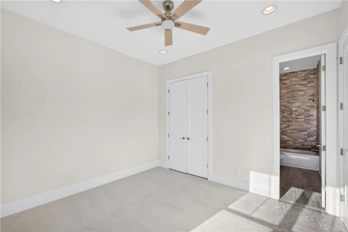 A well-lit bedroom features plush carpeting, a ceiling fan, and convenient access to an adjoining bathroom.