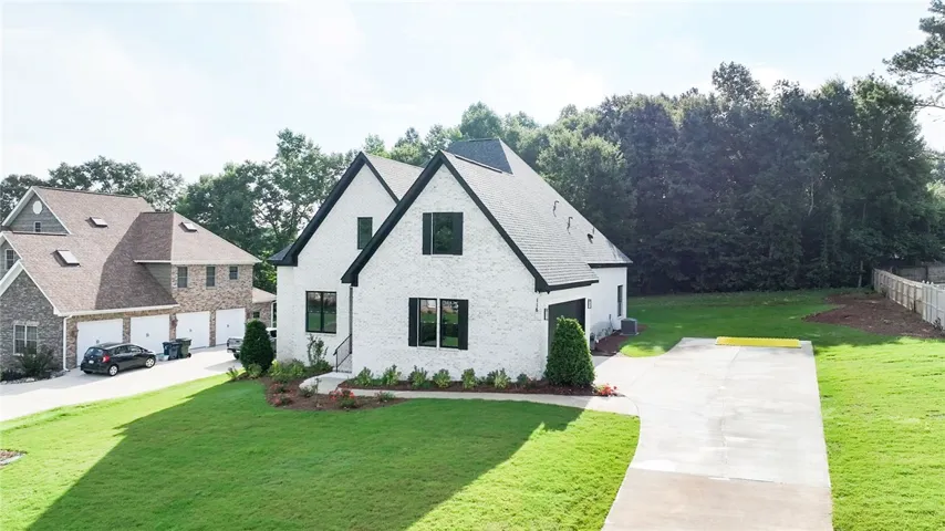 White brick home with black trim boasts a vibrant green lawn and a spacious driveway.