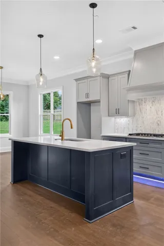 A contemporary kitchen features a spacious central island with a sink, golden faucet, and sleek pendant lighting.