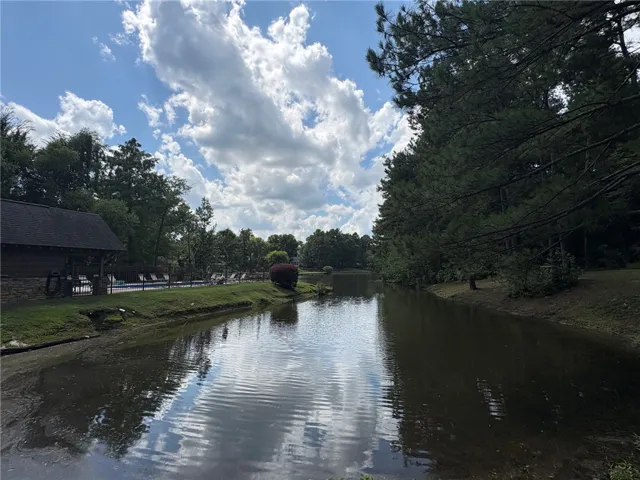A tranquil pond reflecting the sky, bordered by lush trees and a community pool area.