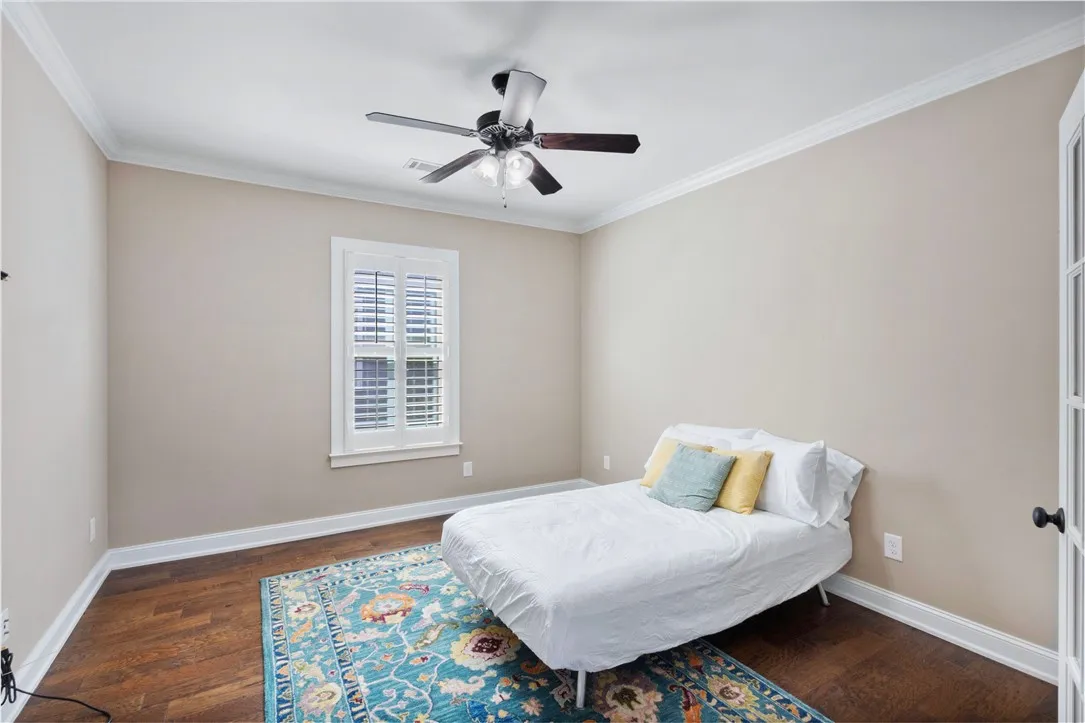 Rich wood flooring and crown molding frame a sun-filled bedroom.
