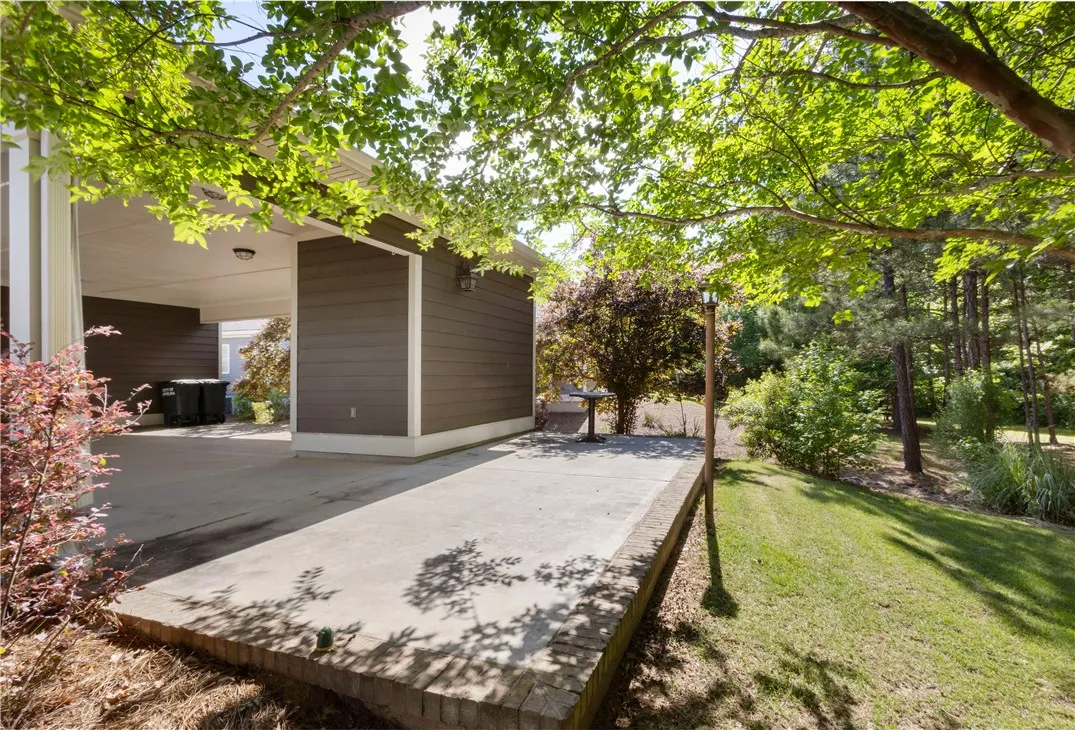 A spacious concrete patio extends from the home's exterior, bordered by lush greenery and mature trees.