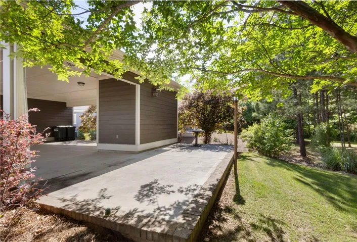 A spacious concrete patio extends from the home's exterior, bordered by lush greenery and mature trees.