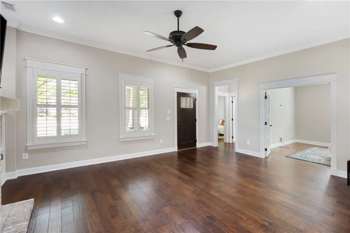 Rich wood floors extend through this ample living space, featuring a classic ceiling fan and abundant natural light.