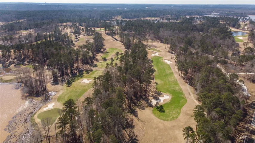 An aerial panorama showcases verdant golf fairways winding through a mature forest, bordered by a tranquil lake.