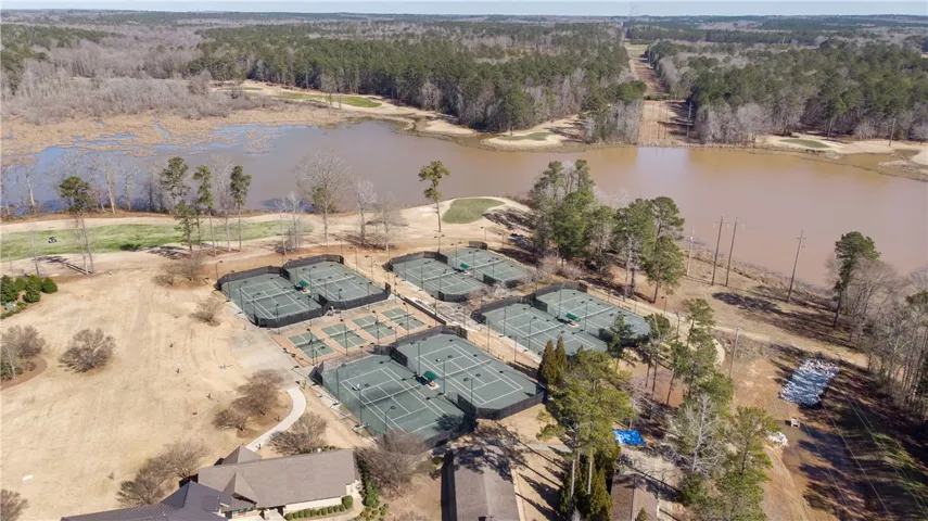 An aerial perspective reveals numerous tennis courts alongside a scenic body of water and wooded areas.