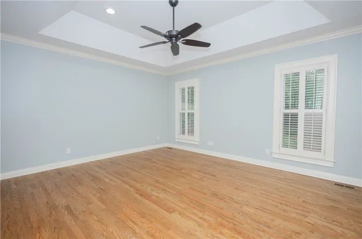Hardwood floors and a tray ceiling define this well-lit primary bedroom.
