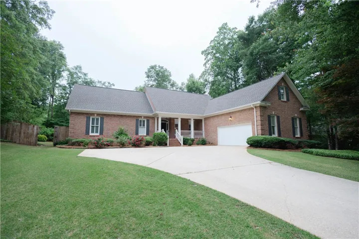 Brick facade home featuring a wide driveway and inviting covered front porch amidst mature trees.