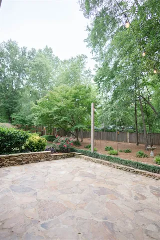 An inviting stone patio unfolds into a beautifully landscaped yard with lush trees and charming string lights.