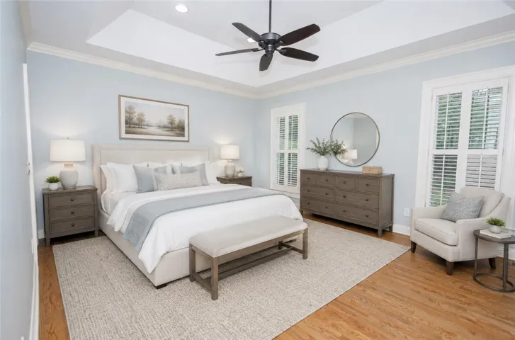 Recessed lighting illuminates a comfortable bedroom featuring a tray ceiling and wood flooring.