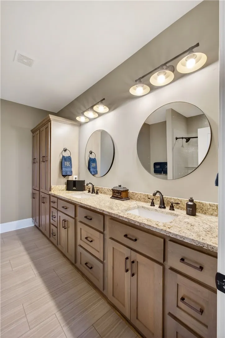 Double vanities with stone counters and modern circular mirrors elevate this well-appointed bathroom.