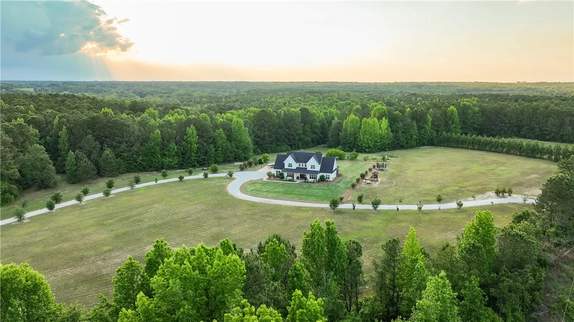 A private, winding driveway leads to a modern farmhouse nestled in a verdant landscape.