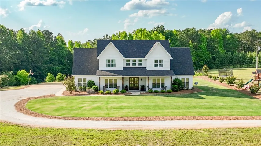 A classic farmhouse design with a deep, inviting porch welcomes you to a verdant landscape.