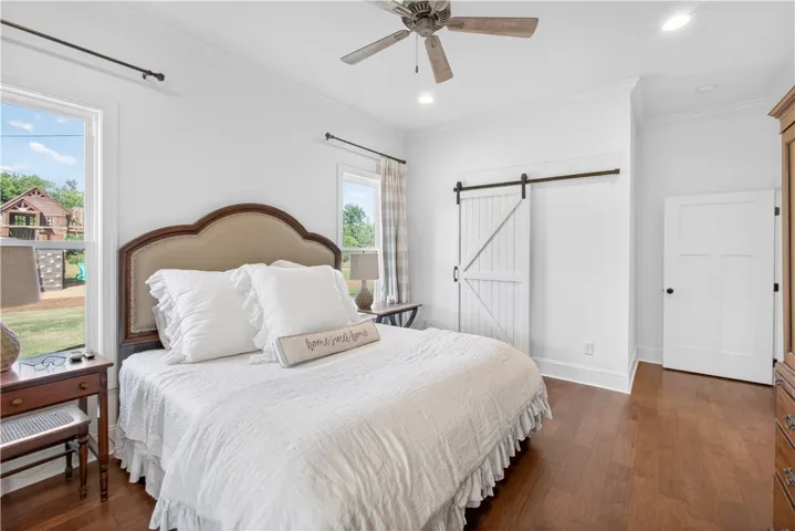 Hardwood floors and a barn door add character to this naturally illuminated bedroom.