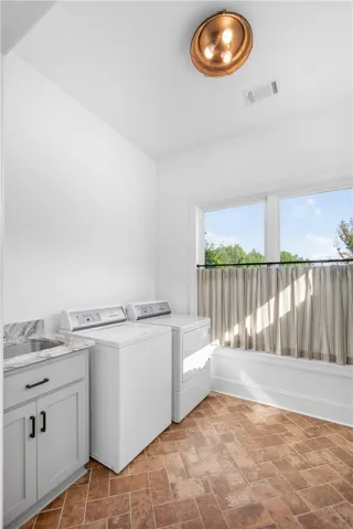 A well-lit utility room features herringbone brick flooring and a functional sink alongside modern laundry appliances.