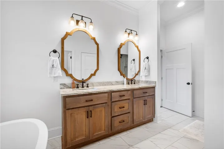 A well-appointed primary bathroom featuring a double vanity with granite counters and stylish wooden cabinetry.