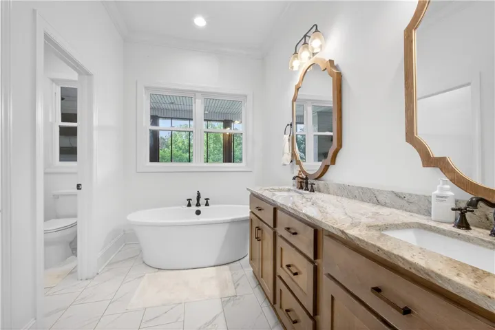A spacious primary bathroom boasts a freestanding tub, dual vanity with granite counters, and light tile flooring.