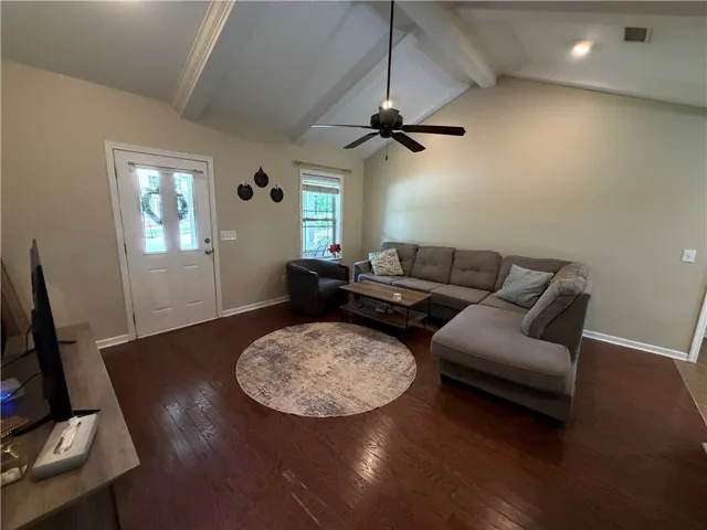 A welcoming living area boasts rich hardwood floors and an inviting vaulted ceiling with exposed beams.