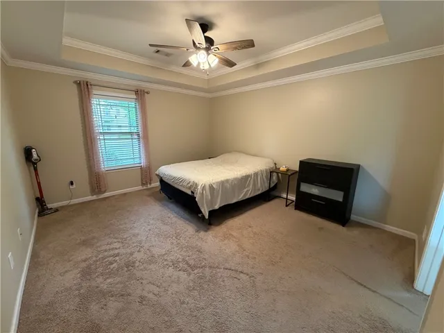 A comfortable bedroom with a tray ceiling and a ceiling fan for year-round comfort.
