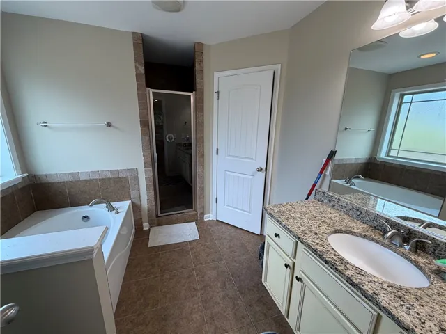A corner soaking tub, separate shower, and dual vanity with stone counters define this well-appointed primary bathroom.