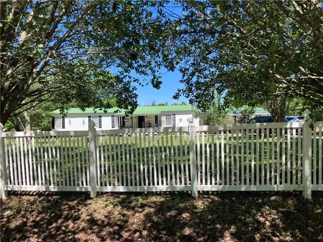 White picket fence encloses a charming residence with a vibrant green roof and welcoming front porch.