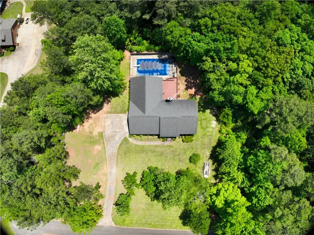 An aerial perspective reveals a private residence nestled amidst verdant foliage with a sparkling pool and a winding driveway.