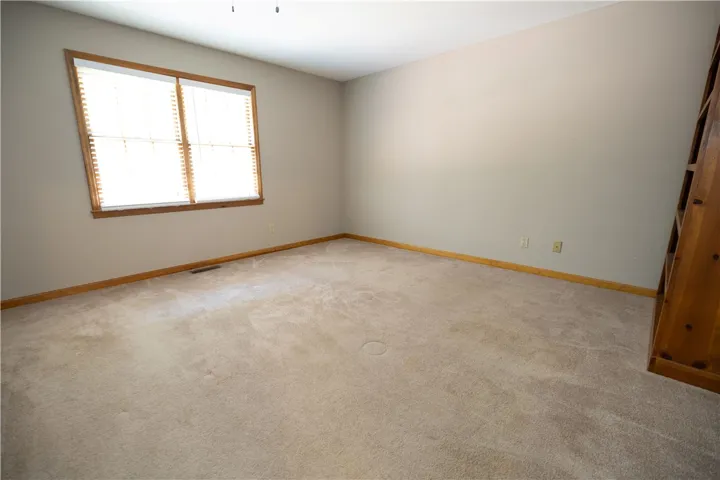 A well-lit, neutral-toned room features broad windows and plush carpeting.