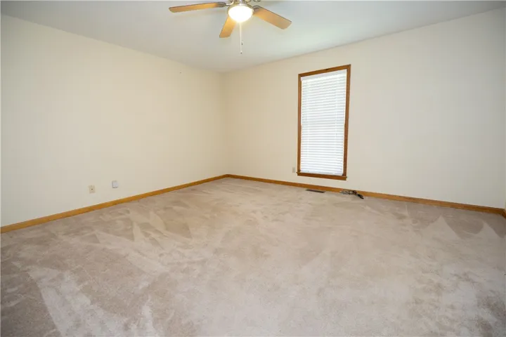 A well-proportioned bedroom with a window offering natural light and comfortable carpeting.