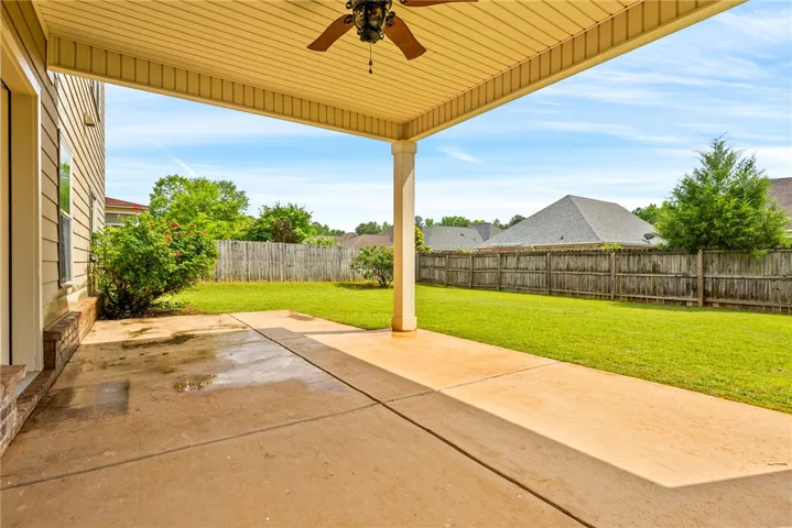 A spacious covered patio extends to a verdant yard, framed by a sturdy wooden fence.