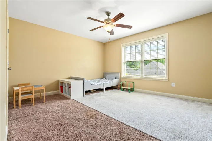 A well-lit bedroom features plush carpeting and a modern ceiling fan.