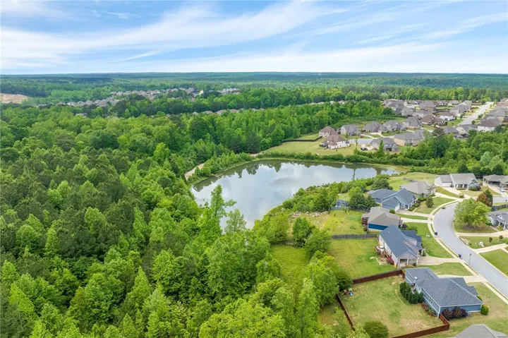 An aerial perspective reveals a serene lake nestled within a verdant forest, adjacent to a charming residential community.