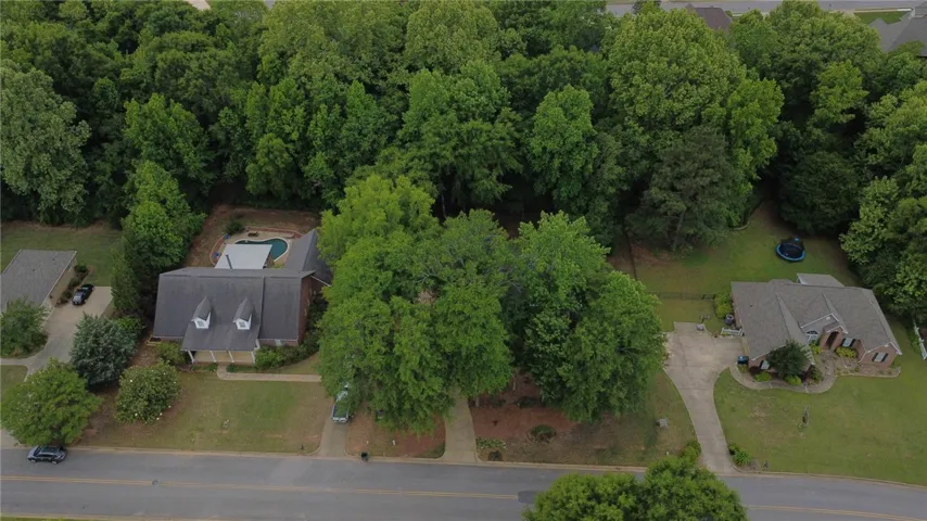 An aerial view showcases a residential property nestled amidst verdant mature trees with a private pool.