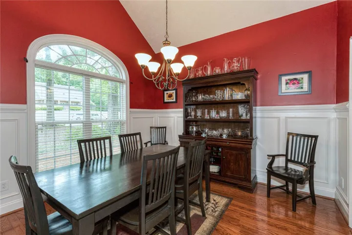 Elegant hardwood flooring enhances this vibrant dining space, illuminated by an arched window and a classic chandelier.