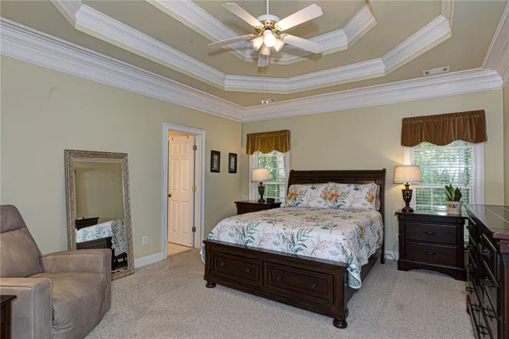 A tray ceiling with crown molding and a ceiling fan defines this peaceful primary bedroom space.