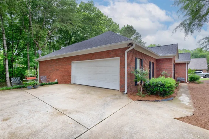 Brick exterior offers an attached garage with a wide concrete driveway, nestled among established trees.