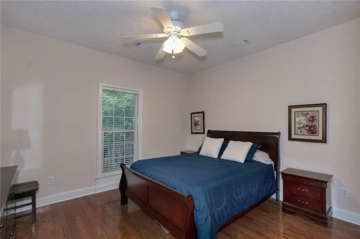 Hardwood floors and a ceiling fan create comfort in this naturally illuminated bedroom.