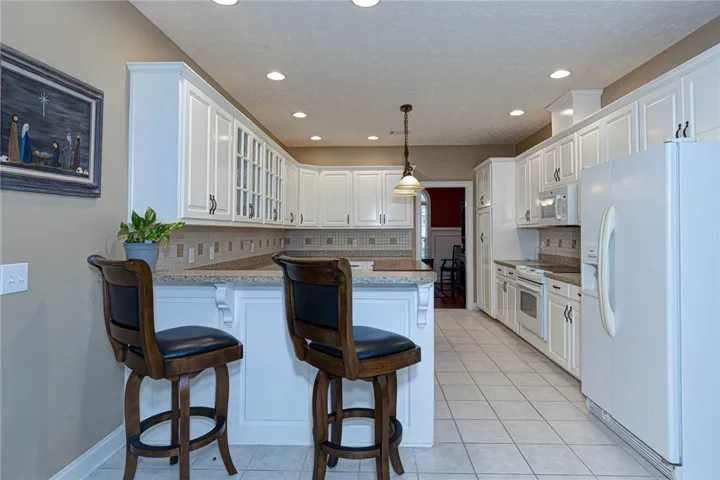 A well-lit kitchen features white cabinetry and a functional breakfast bar.
