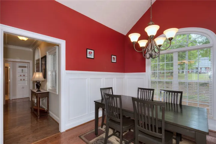 Bold red walls and wainscoting create a captivating dining space, illuminated by a chandelier and a broad arched window.