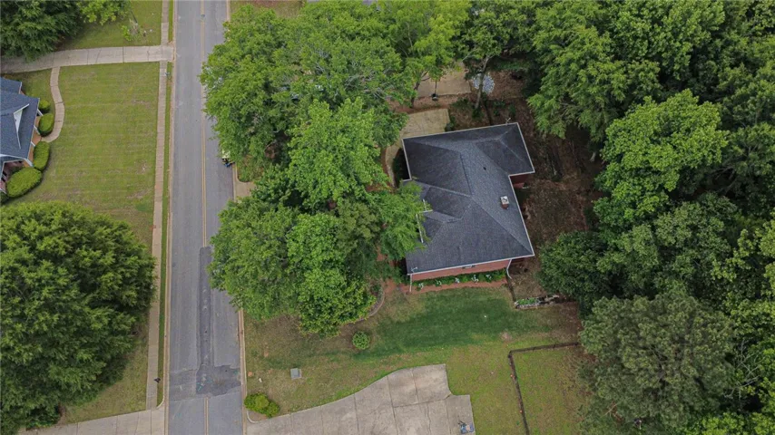 An aerial perspective reveals a private residence nestled amidst mature trees with a well-maintained lawn.