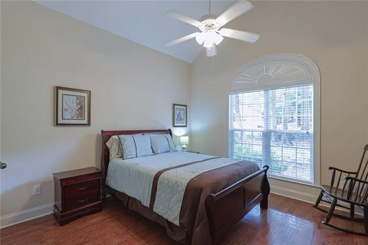 Hardwood floors and a vaulted ceiling elevate this comfortable bedroom with an arched window offering ample light.