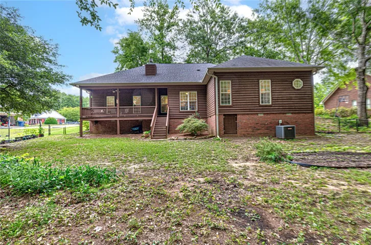 A welcoming rear deck extends from the wood-sided home, framed by lush trees and a sprawling green yard.