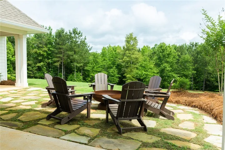 An inviting outdoor gathering spot with flagstone paving and a fire pit, encircled by Adirondack chairs.