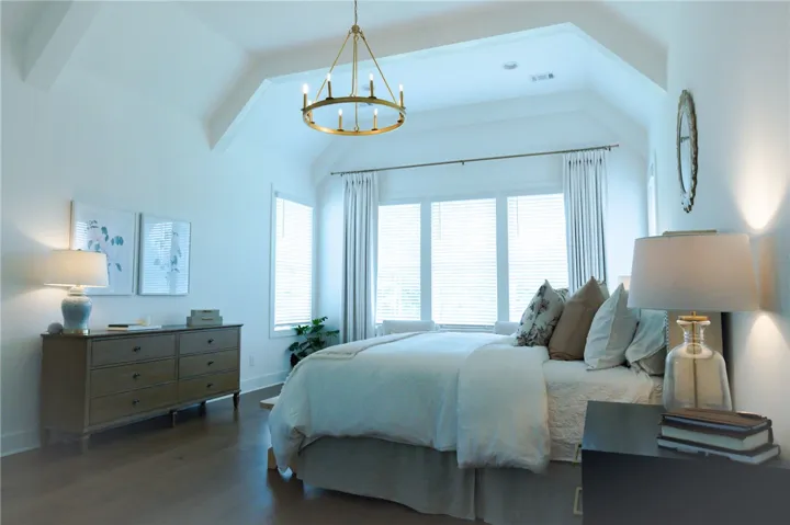 Hardwood floors and a vaulted ceiling complement this primary bedroom's bright window views.